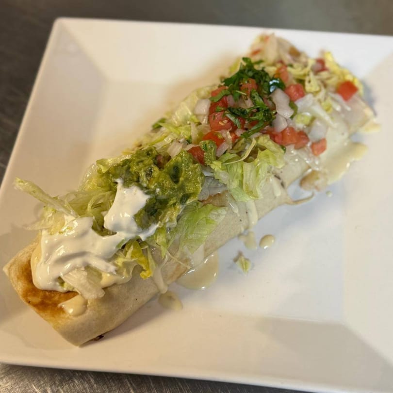 A large burrito topped with lettuce, pico de gallo, guacamole, and sour cream on a white plate.