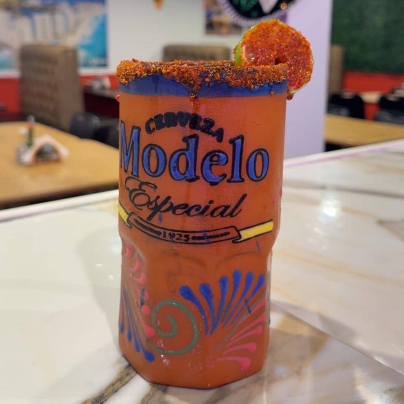 A Modelo Especial michelada in a custom orange glass with a chili-lime rim and lime wedge.