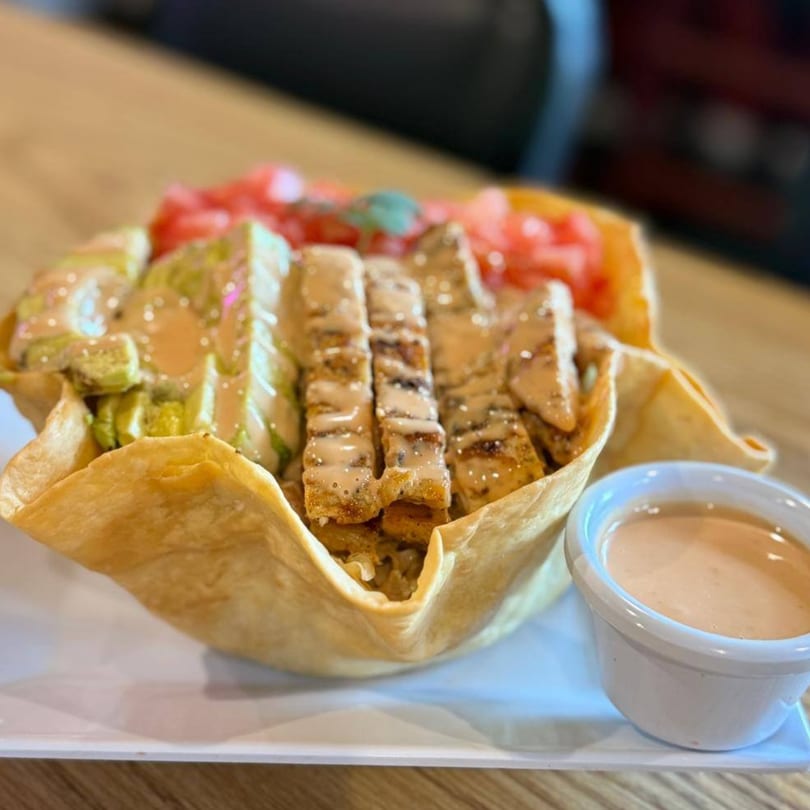 Taco salad in a crispy tortilla bowl with grilled chicken, lettuce, tomatoes, and dressing.